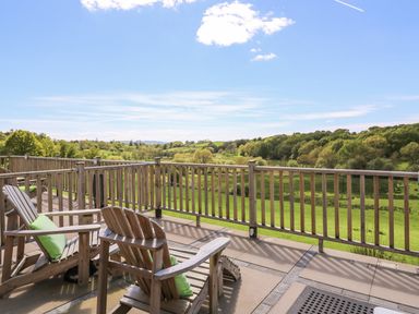 A wooden deck with chairs overlooking green fields and trees at Foxes Meadow in Howey near Llandrindod Wells