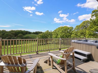 An outdoor patio with wooden chairs hot tub and a view of green fields and trees at Foxes Meadow in Howey near Llandrindod Wells
