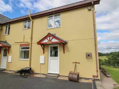 The exterior of a beige house with a white door and windows and garden tools outside at Foxes Meadow in Howey near Llandrindod Wells