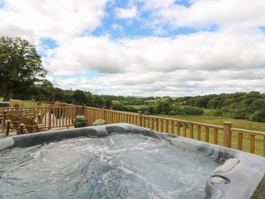 An outdoor hot tub on a wooden deck overlooking green fields and trees at Foxes Meadow in Howey near Llandrindod Wells