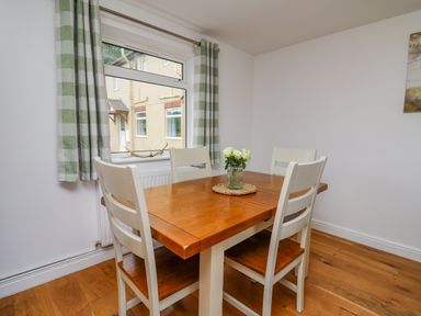 A dining area with a wooden table and four chairs next to a window with checkered curtains at Foxes Meadow in Howey near Llandrindod Wells
