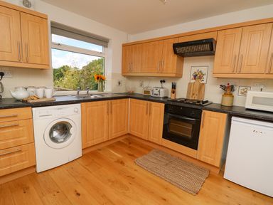 A kitchen with wooden cabinets a washing machine an oven a microwave and a window with sunflowers at Foxes Meadow in Howey near Llandrindod Wells
