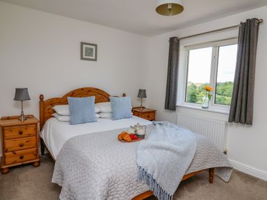 A bedroom with a wooden bed with blue pillows and a tray with croissants and tea by a window at Foxes Meadow in Howey near Llandrindod Wells