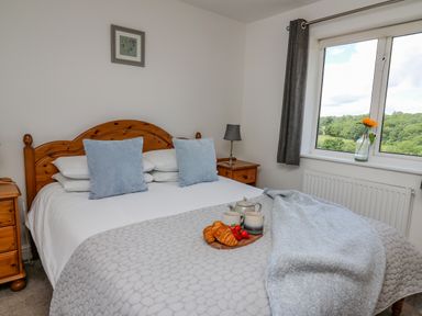 A bedroom with a wooden bed frame and two pillows beside a window with curtains at Foxes Meadow in Howey near Llandrindod Wells