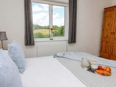 A bedroom with a bed and breakfast items on it by a window with curtains and a wooden wardrobe at Foxes Meadow in Howey near Llandrindod Wells
