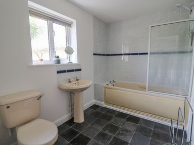 A bathroom with a beige toilet sink and bathtub with a shower screen and a window above at Foxes Meadow in Howey near Llandrindod Wells