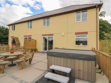 A fenced outdoor patio with wooden table and chairs and a covered hot tub at Pheasant Wood in Howey near Llandrindod Wells