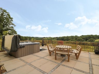 An outdoor patio with a hot tub a round wooden table with benches and a view of trees and hills at Pheasant Wood in Howey near Llandrindod Wells