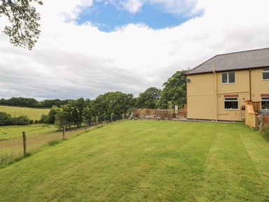 A backyard with a green lawn next to a yellow house and trees at Pheasant Wood in Howey near Llandrindod Wells