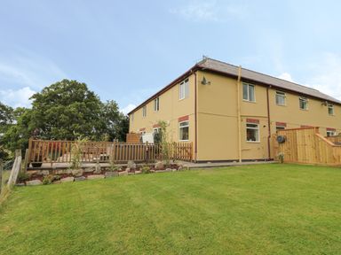 A beige two-story house with a fenced patio and a green lawn with trees at Pheasant Wood in Howey near Llandrindod Wells