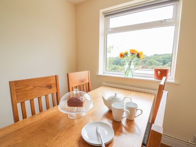 A dining table with a teapot cups a plate with a knife and a cake under a glass dome by a window with flowers at Pheasant Wood in Howey near Llandrindod Wells