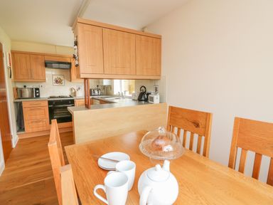 A kitchen area with wooden cabinets and countertop next to a dining table with cups teapot and cake cover at Pheasant Wood in Howey near Llandrindod Wells