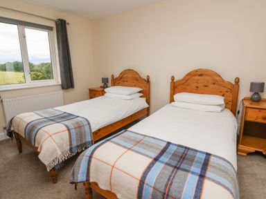 A bedroom with two single beds with plaid blankets and wooden headboards at Pheasant Wood in Howey near Llandrindod Wells