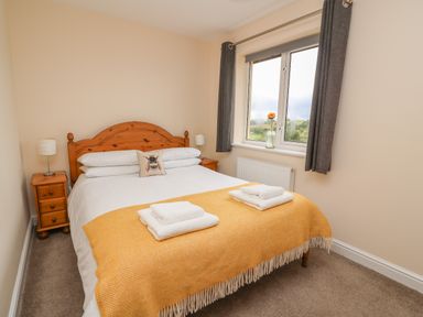 A bedroom with a wooden bed frame two bedside tables and a window with dark curtains at Pheasant Wood in Howey near Llandrindod Wells