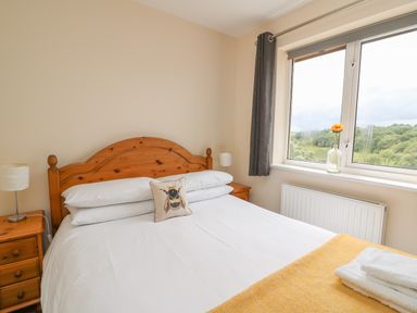 A bedroom with a wooden bedframe white bedding bedside tables with lamps and a window with a flower at Pheasant Wood in Howey near Llandrindod Wells