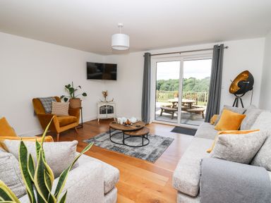 A living room with a gray sofa and armchair a wooden coffee table and sliding glass doors at Pheasant Wood in Howey near Llandrindod Wells