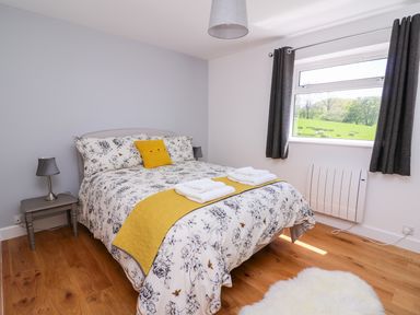 A bedroom with a bed a bedside table lamps a window with curtains and wooden flooring at Owl Cottage in Llandrindod Wells