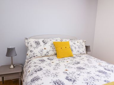 A bed with floral bedding and a yellow pillow between two bedside tables with lamps at Owl Cottage in Llandrindod Wells