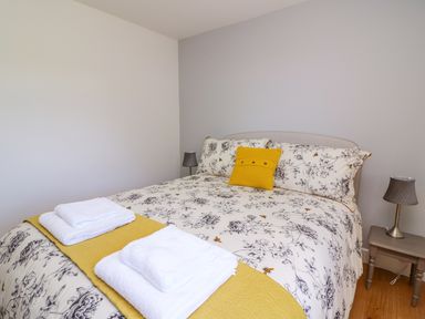 A bedroom with a double bed covered in floral bedding and a yellow cushion with two bedside tables and lamps at Owl Cottage in Llandrindod Wells