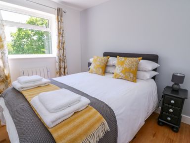 A bedroom with a double bed with yellow and grey pillows and blankets next to a bedside table with a lamp at Owl Cottage in Llandrindod Wells