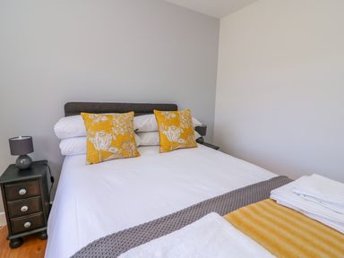 A bedroom with a bed with white sheets and yellow floral pillows next to a bedside table with a lamp at Owl Cottage in Llandrindod Wells