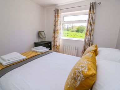 A bedroom with a bed folded towels bedside table with mirror and floral curtains at Owl Cottage in Llandrindod Wells