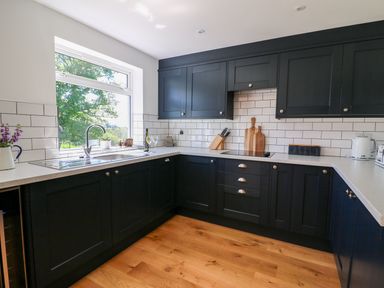 A kitchen with black cabinets white countertops a window and wooden floor at Owl Cottage in Llandrindod Wells