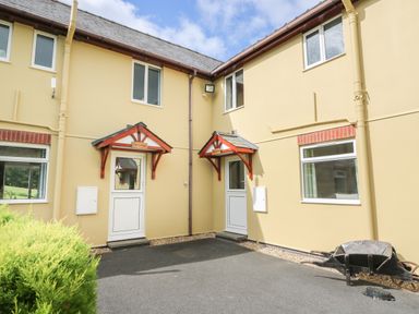 The exterior of a beige building with two white doors under wooden canopies and several windows with a paved area and a wheelbarrow near the wall at Owl Cottage in Llandrindod Wells