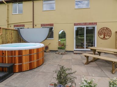 A backyard patio with a wooden hot tub a picnic table sliding glass door and decorative wall art at Owl Cottage in Llandrindod Wells