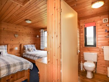 A twin bedroom with checked bedding and a bathroom with a toilet separated by a wooden door at Wildcat Lodge in Newtonmore