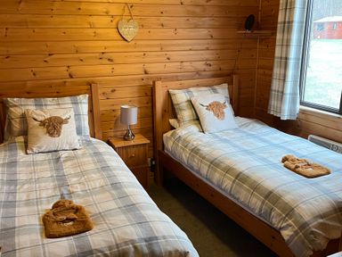 A bedroom with two single beds with checked bedding and animal face pillows at Wildcat Lodge in Newtonmore