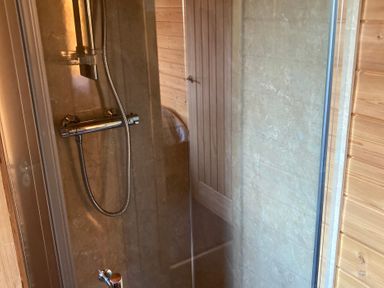 A shower area with a handheld showerhead and glass door in a wooden room at Wildcat Lodge in Newtonmore