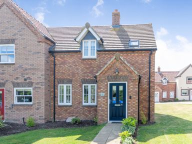 Front view of a brick house with white framed windows and blue door with pathway and grass at Lilipad Cottage The Bay near Filey