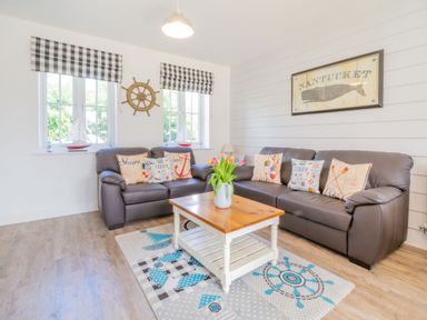 A living room with two brown leather sofas, a wooden coffee table, nautical cushions, wall decoration of a whale and ship wheel, at Lilipad Cottage in The Bay near Filey