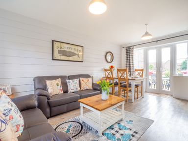 A living room with two brown sofas a wooden coffee table dining table with four chairs and glass doors at Lilipad Cottage The Bay near Filey