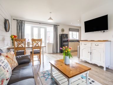 An open plan living room and kitchen with a dining table set chairs and flowers on a coffee table at Lilipad Cottage in The Bay near Filey