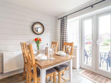 A dining room with wooden table and chairs set with plates and glasses near glass doors at Lilipad Cottage The Bay near Filey
