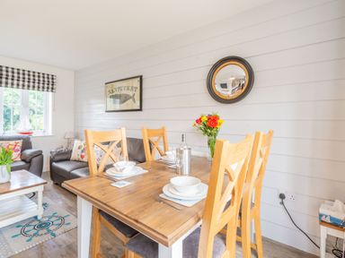 A dining table set with plates and glasses beside a living area with leather sofas and a window with checkered blinds at Lilipad Cottage in The Bay near Filey