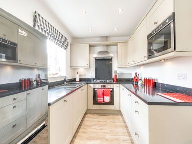 A kitchen with cream cabinets black countertops and red kitchen accessories at Lilipad Cottage The Bay near Filey