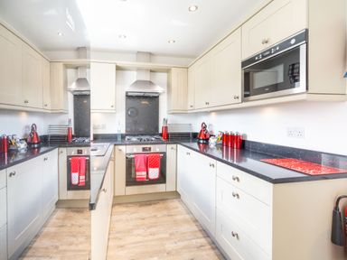 A kitchen with beige cabinets black countertops red accessories and wooden floor at Lilipad Cottage The Bay near Filey