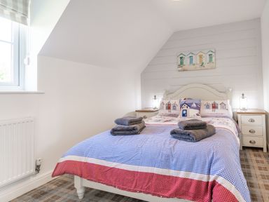 A bedroom with a double bed with patterned bedding and towels on top and two nightstands with lamps at Lilipad Cottage in The Bay near Filey