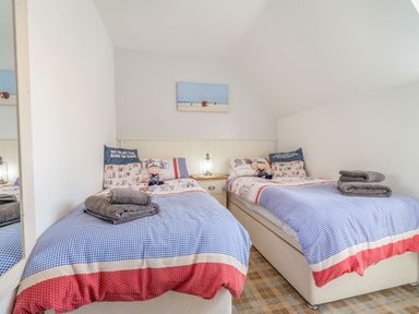 A bedroom with two single beds with blue checked bedding and folded towels at Lilipad Cottage in The Bay near Filey