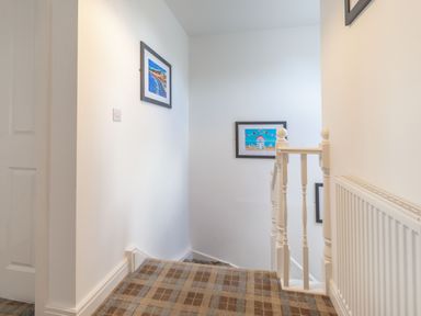 A hallway with carpeted stairs and framed pictures on the walls at Lilipad Cottage The Bay near Filey