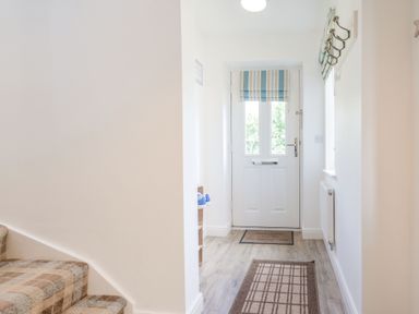 A hallway with a front door a patterned rug a coat rack and carpeted stairs at Lilipad Cottage in The Bay near Filey