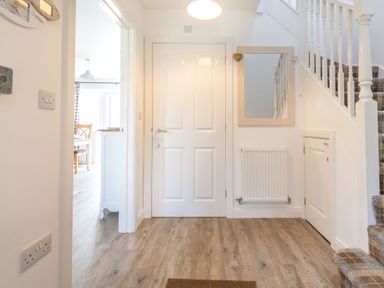 A hallway with a white door a staircase with carpeted steps a wall mirror radiator and a view into a dining area at Lilipad Cottage The Bay near Filey
