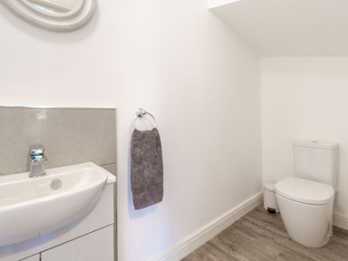 A bathroom with a sink and towel on a ring and a toilet with a small trash bin on a wooden floor at Lilipad Cottage in The Bay near Filey