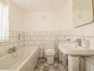 A bathroom with a bathtub toilet and sink with patterned floor tiles at The Beach Halt in Perranporth