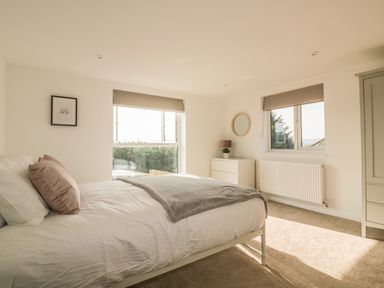 A bedroom with a bed a dresser a mirror and two windows at The Beach Halt in Perranporth
