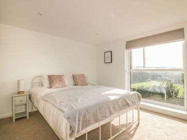 A bedroom with a white metal bed frame two bedside tables and a large window showing a green outdoor view at The Beach Halt in Perranporth