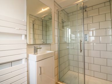 A bathroom with a glass shower enclosure a white sink with cabinet and a rectangular mirror at The Beach Halt in Perranporth